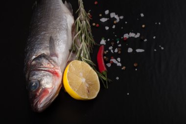 Taze balık, limon, biber ve biberiye siyah bir arka plan. Ti