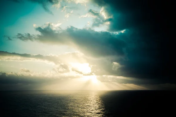 Dramatic sunset rays through a cloudy dark sky over the ocean. T