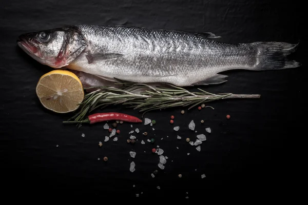 Peixe-marinho fresco deitado no fundo escuro com especiarias. Espaço para t — Fotografia de Stock