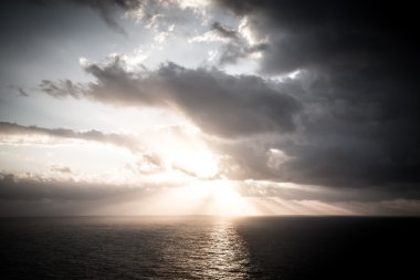 Okyanusun üzerindeki bulutlu karanlık gökyüzünde dramatik gün batımı ışınları 