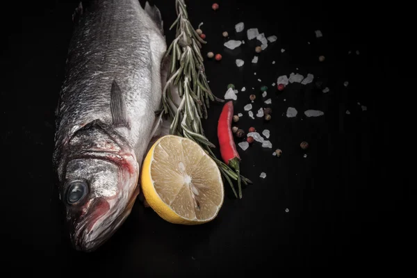 Ikan segar, lemon, lada dan rosemary pada latar belakang hitam — Stok Foto