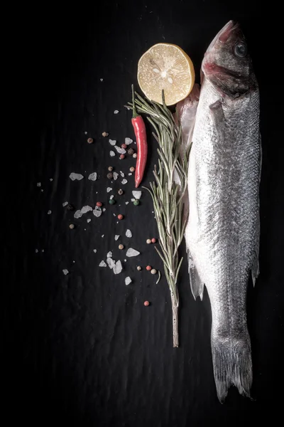 Frischer Fisch, Zitrone, Pfeffer und Rosmarin auf schwarzem Hintergrund. ti — Stockfoto