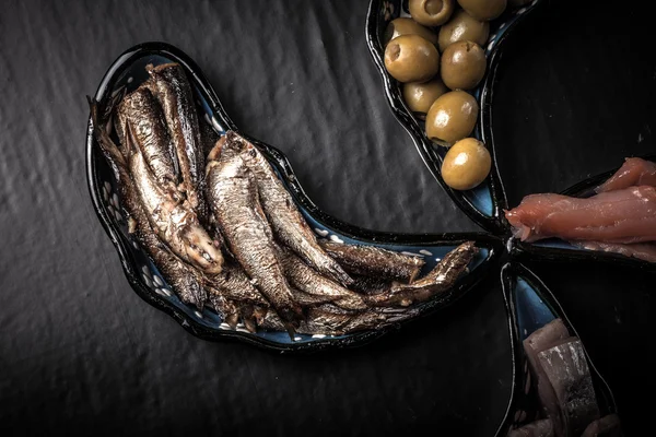 Ассортимент рыбы и оливки на волшебных тарелках на темном фоне — стоковое фото