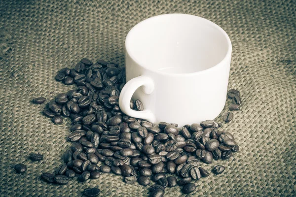 Kávová zrna a prázdný bílý šálek na vyhození pozadí. tinte — Stock fotografie