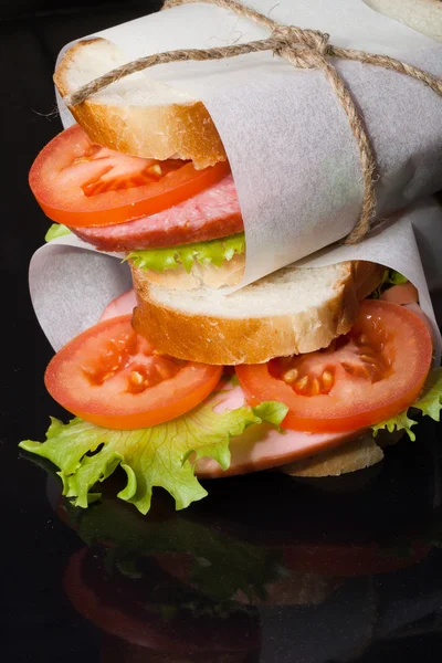 Sandwich with sausage bandaged twine on a black background. — Stock Photo, Image
