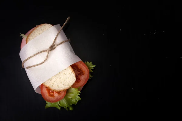 Бутерброд з ковбасою, перев'язаний шпагатом на чорному тлі. За допомогою — стокове фото
