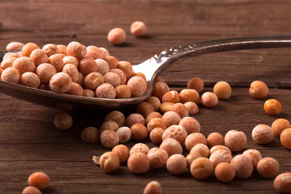 Pois secs dans une cuillère en argent sur une table en bois. teinté — Photo