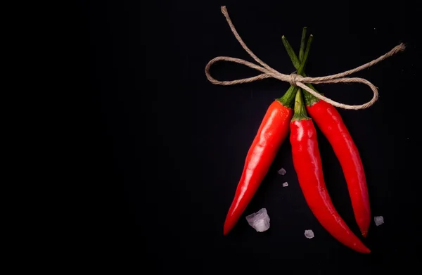 Verwante hot rode chili peppers en een groot kristal zout op een donker — Stockfoto