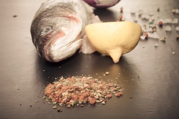 生の魚、タマネギ、レモンと黒いテーブルの上のスパイス。トーン — ストック写真