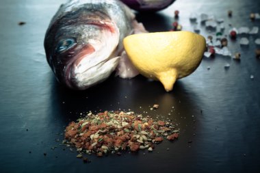 Çiğ balık, soğan, limon ve baharat siyah bir tablo. Tonda