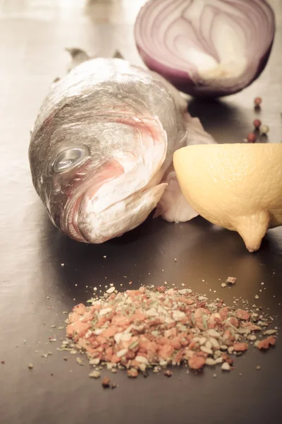 Roher Fisch, Zwiebeln, Zitrone und Gewürze auf einem schwarzen Tisch. gemildert — Stockfoto