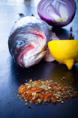 Çiğ balık, soğan, limon ve baharat siyah bir tablo. Tonda