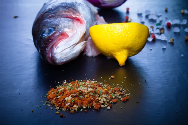 Roher Fisch, Zwiebeln, Zitrone und Gewürze auf einem schwarzen Tisch. gemildert — Stockfoto