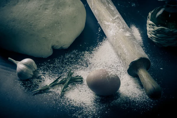 Dough on a black board with flour. olive oil, eggs, rolling pin, — Stock Photo, Image
