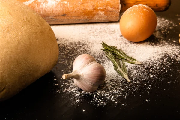 Dough on a black board with flour. eggs, rolling pin, garlic. Ti — Stock Photo, Image