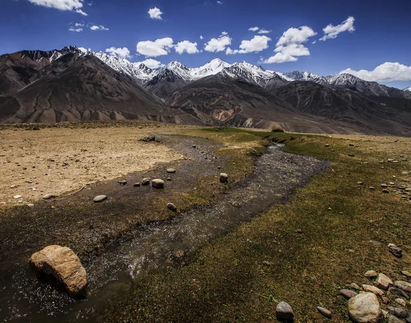 The rapid stream in the valley and snow-capped peaks of the moun — Stock Photo, Image