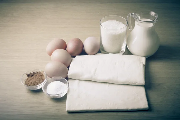 Milch, Zucker, Kakao, Blätterteig, Eier und Salz auf einem Holzbrett. — Stockfoto