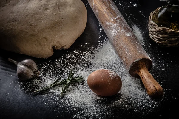 Dough on a black board with flour. olive oil, eggs, rolling pin, — Stock Photo, Image