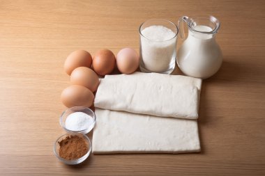 Süt, şeker, kakao, puf hamur, yumurta ve tuz bir ahşap tahta üzerinde.