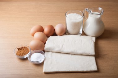 Süt, şeker, kakao, puf hamur, yumurta ve tuz bir ahşap tahta üzerinde.