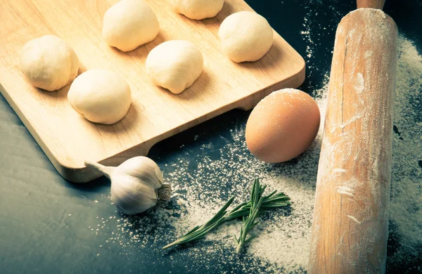 Garlic, rosmary, egg, rolling pin and pieces of dough on the woo — Stock Photo, Image