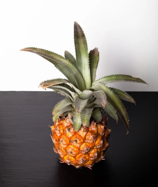 Piña entera fresca sobre una mesa negra cerca de la pared blanca — Foto de Stock