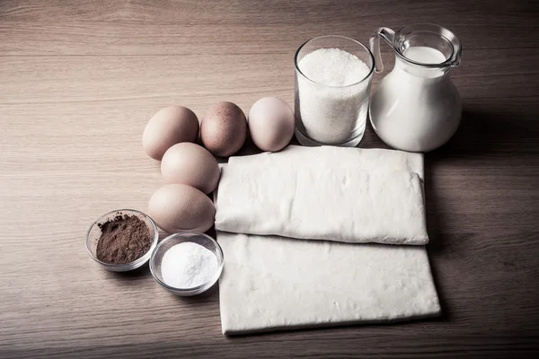 Mléko, cukr, kakao, listového těsta, vejce a sůl na dřevěném prkénku. — Stock fotografie