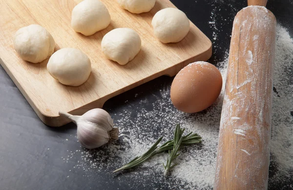 Garlic, rosmary, egg, rolling pin and pieces of dough on the woo — Stock Photo, Image