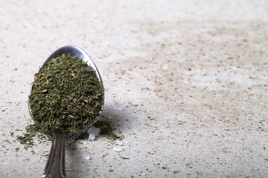 Spoon with dried herb and salt on the stone background