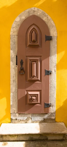 Old wooden door with metal hinges and lock on the yellow wall — Stock Photo, Image