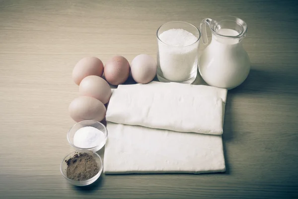 Latte, zucchero, cacao, pasta sfoglia, uova e sale su una tavola di legno . — Foto Stock