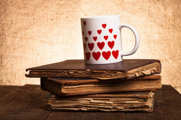 Old books and mug with many pictured hearts on the old wooden ta — Stock Photo, Image