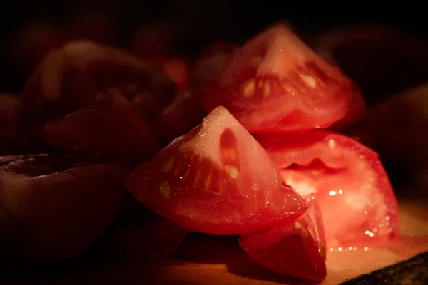 Trozos de tomate en una tabla de madera. Bajo nivel de luz y poca profundidad — Foto de Stock