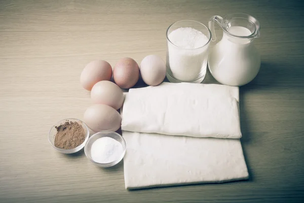 Latte, zucchero, cacao, pasta sfoglia, uova e sale su una tavola di legno . — Foto Stock