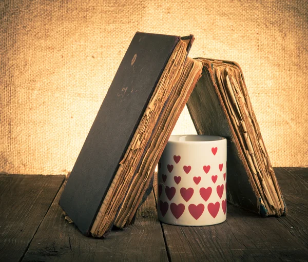 Old books and mug with many pictured hearts on the old wooden ta — Stock Photo, Image