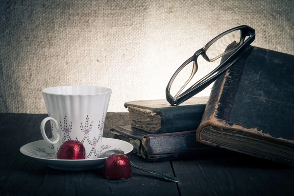Чашка кофе, шоколад, стаканы и стопка старых книг на o — стоковое фото