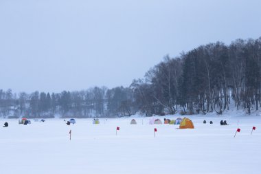 Many flags and tents on the snow-covered field near the forest clipart