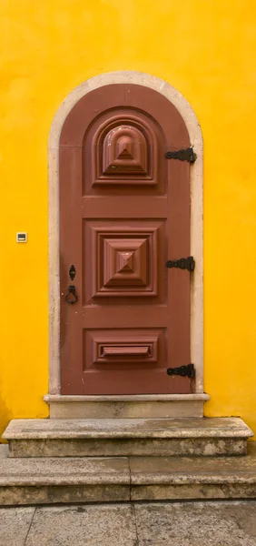 Porta de madeira velha com dobradiças de metal e bloqueio na parede amarela — Fotografia de Stock