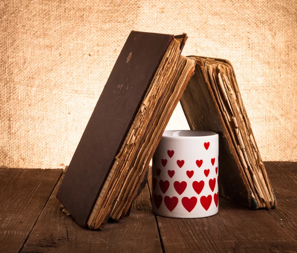 Alte Bücher und Becher mit vielen abgebildeten Herzen auf der alten Holztafel — Stockfoto