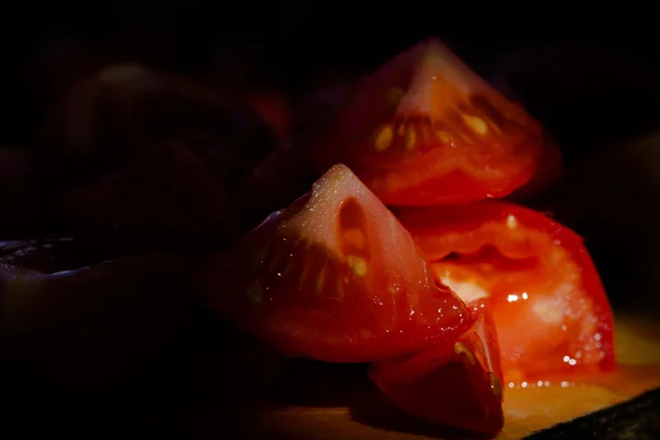 Trozos de tomate en una tabla de madera. Bajo nivel de luz y poca profundidad — Foto de Stock