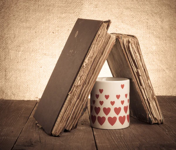 Старые книги и кружка со многими изображенными сердцами на старой деревянной тарелке — стоковое фото