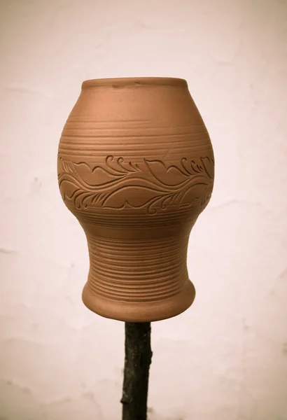 Clay pot with a pattern on a wooden stick on a light background. — Stock Photo, Image