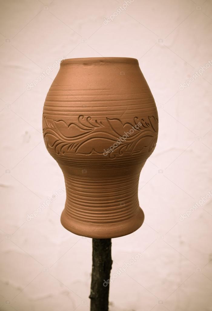 Clay pot with a pattern on a wooden stick on a light background.