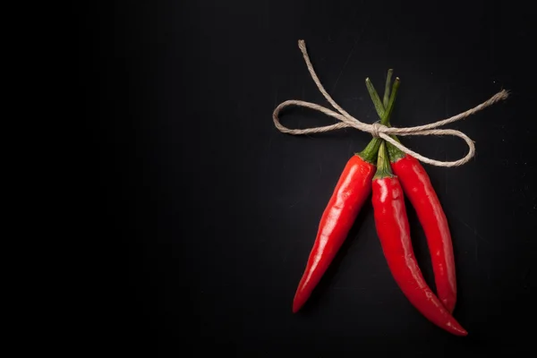 Drie hete rode chili peper gerelateerde door bindgaren met op een zwarte rug — Stockfoto