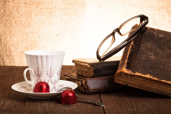 Cup of coffee, shokolad, glasses and stack of old books on the o — Stock Photo, Image