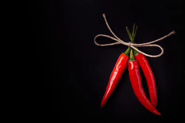 Drie hete rode chili peper gerelateerde door bindgaren met op een zwarte rug — Stockfoto