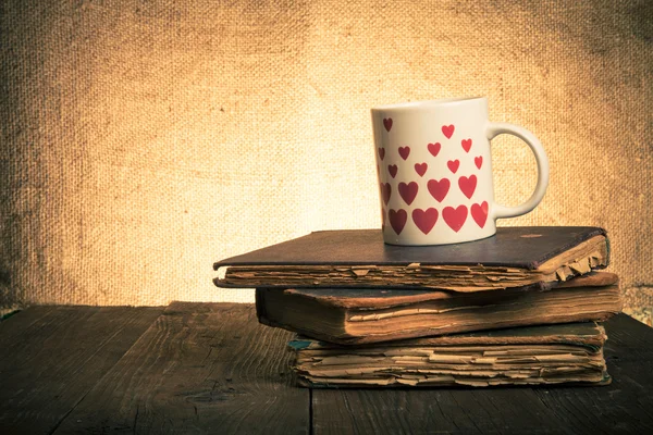 Старые книги и кружка со многими изображенными сердцами на старой деревянной тарелке — стоковое фото