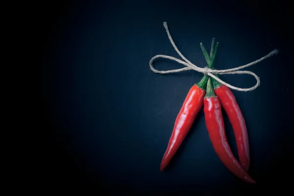 Three hot red chili pepper related by twine with on a black back — Stock Photo, Image