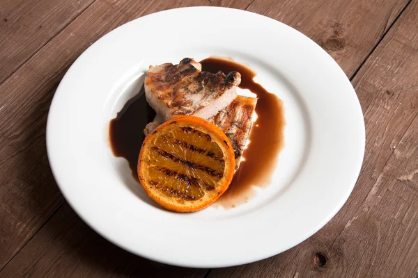 Carne alla griglia con arancia su piatto di ceramica bianca su vecchia ta di legno — Foto Stock