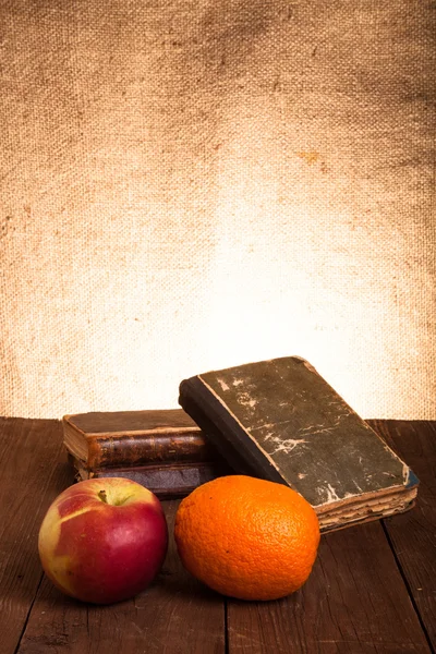 Still life with apple, orange and a stack of old books on old wo — Stock Photo, Image